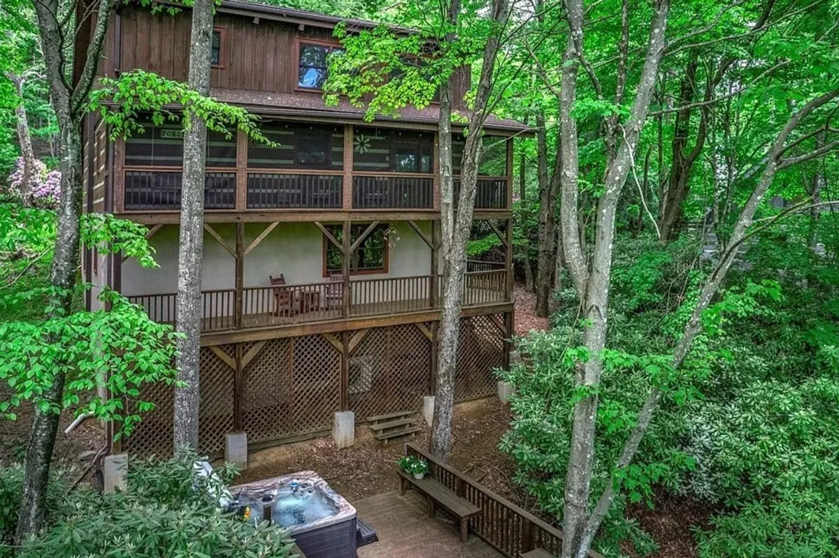 A cozy exterior shot of a wooden cabin set against a backdrop of rich foliage, featuring a hot tub on the deck and comfortable seating. The image evokes a sense of immersion in nature, with the hot tub perfectly positioned for stargazing or soaking after outdoor pursuits.