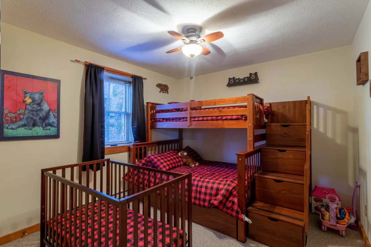 A cheerful bunk bedroom is shown with twin-over-full bunk beds, a crib, bear artwork, and colorful bedding. The room has a playful, inviting atmosphere, ideal for children to play, sleep, and dream up adventures.