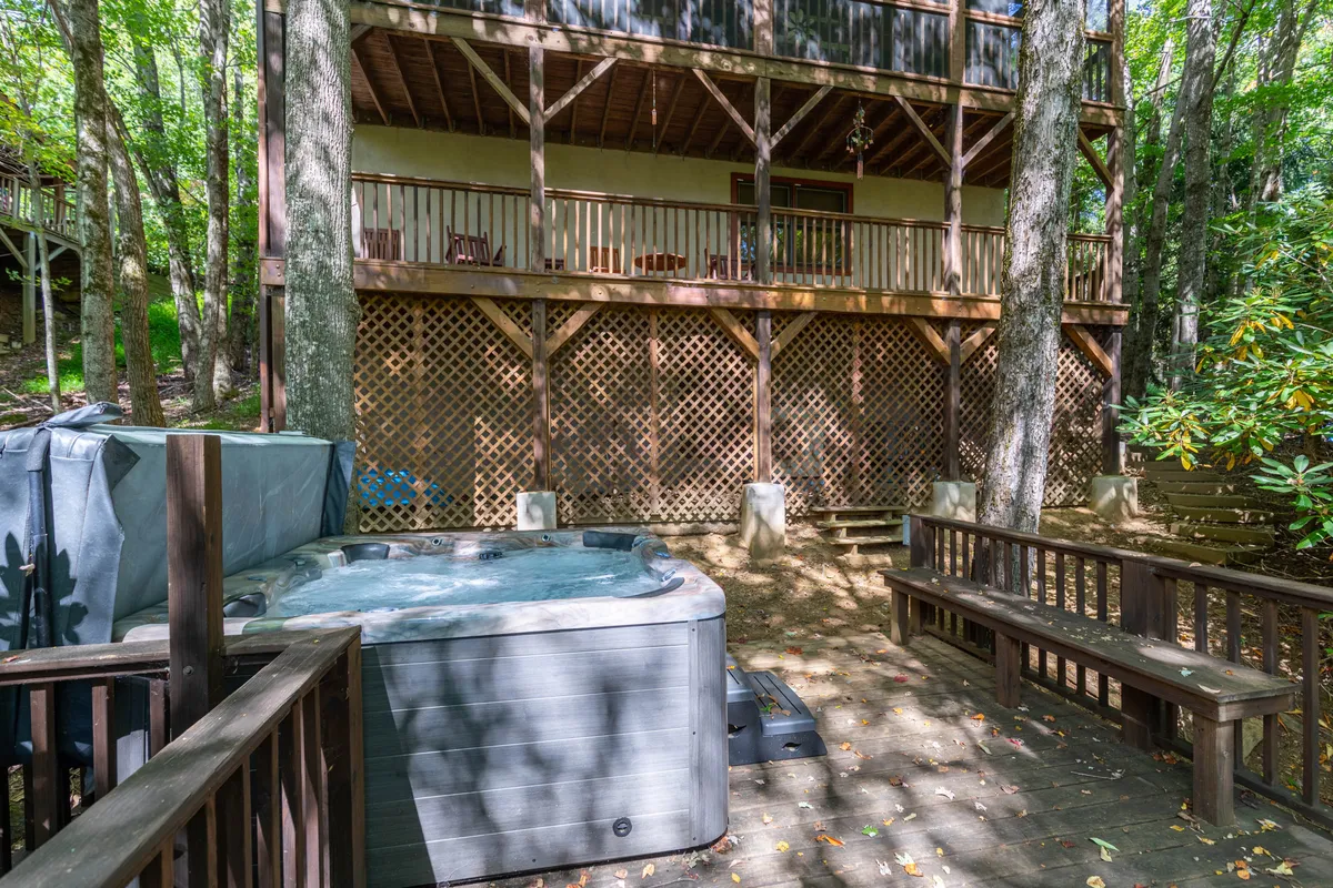 This inviting image features a hot tub on a spacious wooden deck bordered by trees and a balcony above. The tranquil setting is perfect for human relaxation while dogs rest nearby after an exciting day outdoors.