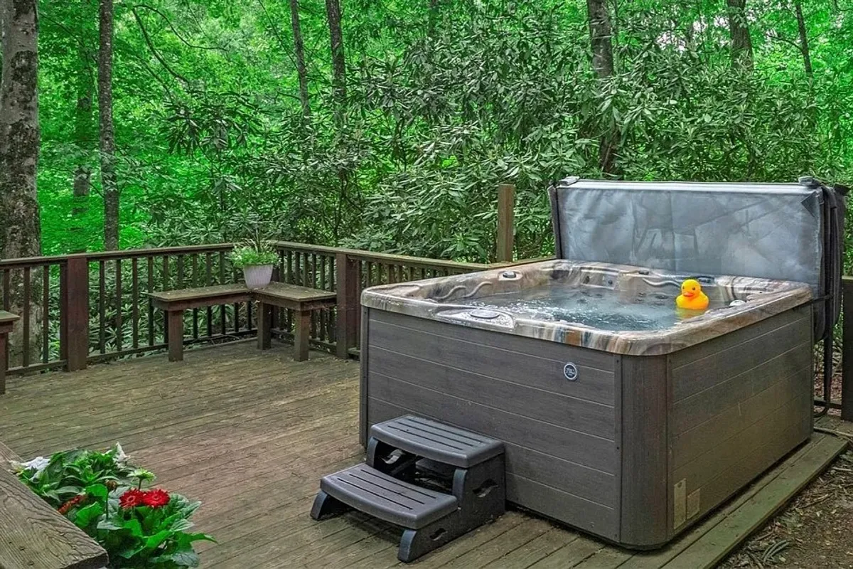 A soothing hot tub sits on a wooden deck, bordered by lush greenery. A playful rubber duck floats in the water, and the deck offers space for gathering with family or friends, enjoying nature, and relaxing after a day of activities.