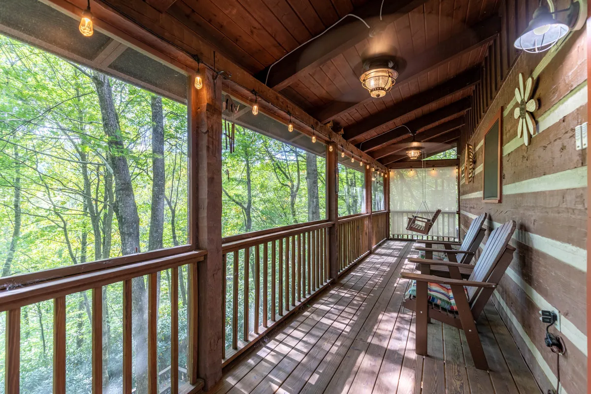 This serene exterior shot features a wooden deck with comfortable swing chairs, hanging lights, and abundant natural light. Surrounded by trees, it invites relaxation, reading, and group conversations in a tranquil outdoor setting.