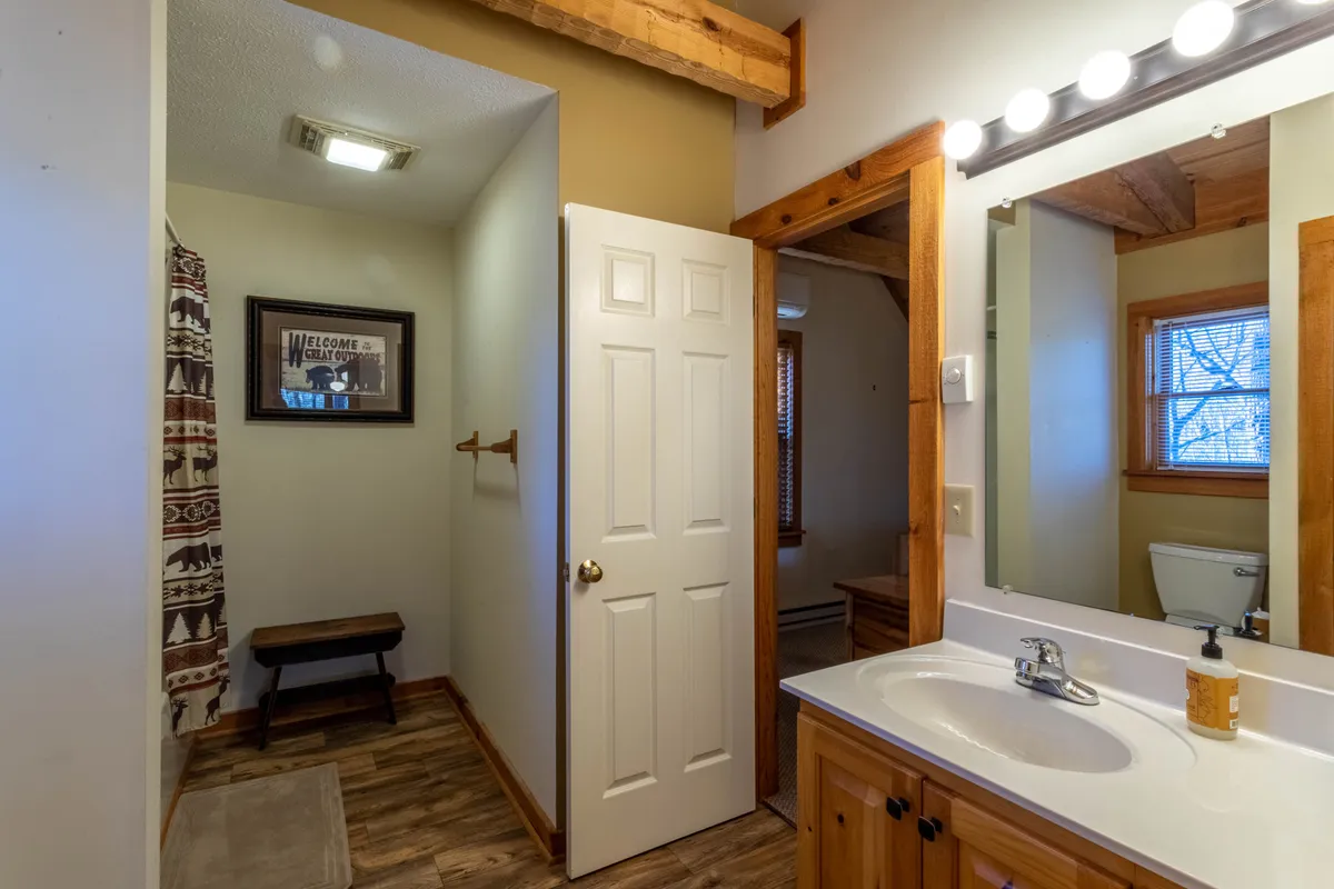 A well-lit downstairs bath features a vanity sink, mirror, wooden accents, and a shower curtain. The space feels comfortable and practical, suitable for family routines and offering privacy and convenience.