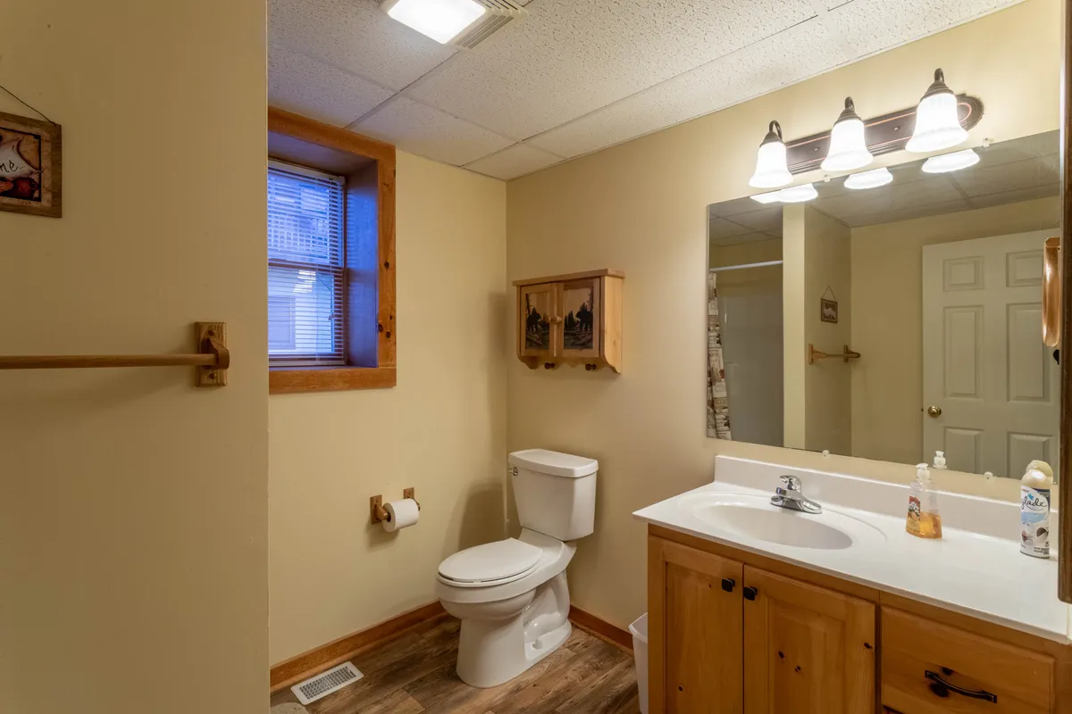 A well-lit full bath with a vanity, sink, toilet, and wooden cabinetry. Morning sunlight filters through the window, creating a refreshing and calm mood ideal for preparing for the day or relaxing after activities.