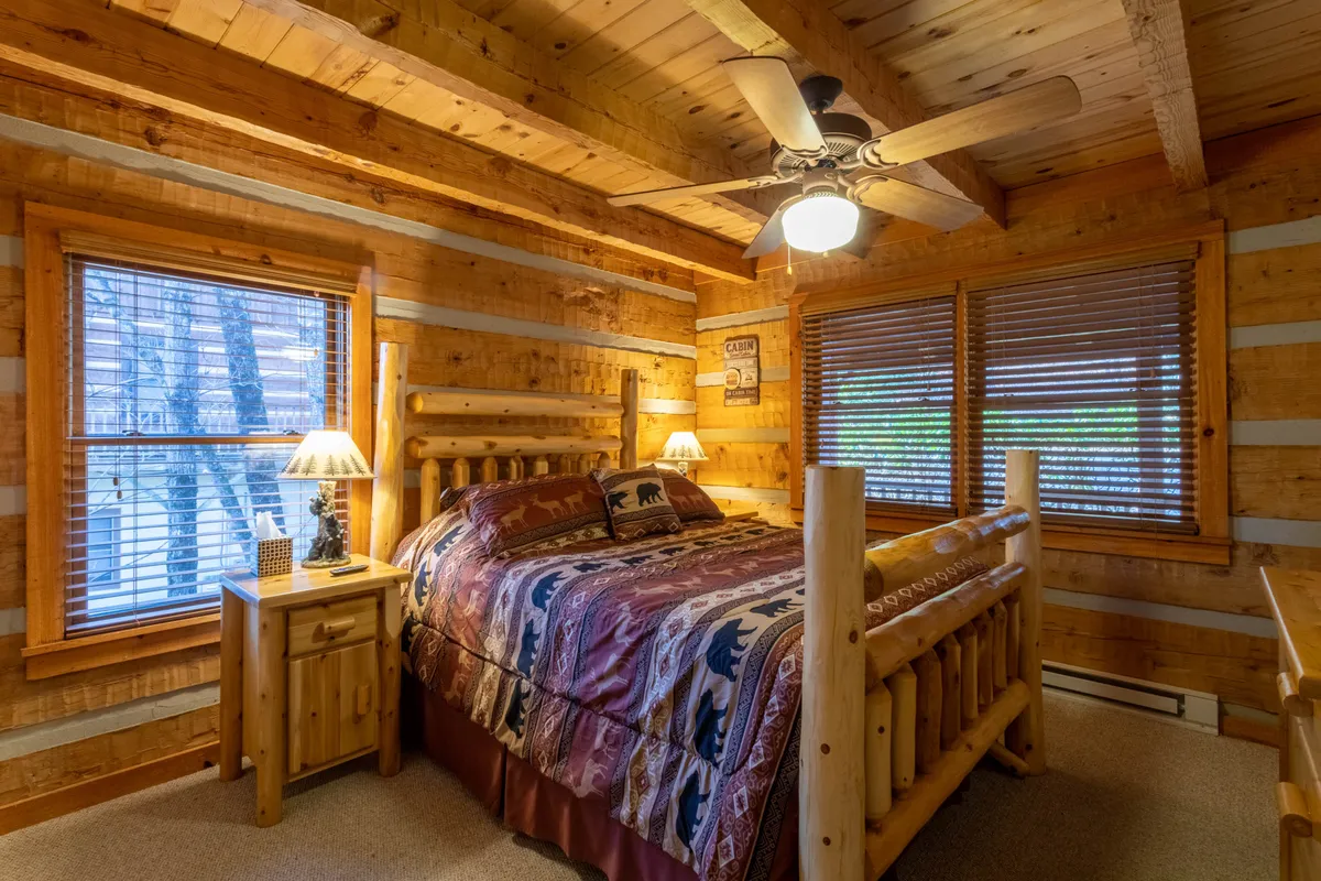 This image showcases a log bed surrounded by wooden walls, soft lamps, and windows that allow nature views to pour in. The room exudes a warm and inviting atmosphere, perfect for restful sleep after a day of mountain activities. The cozy textures and natural light highlight the sense of comfort and relaxation, aligning with the suite's theme.