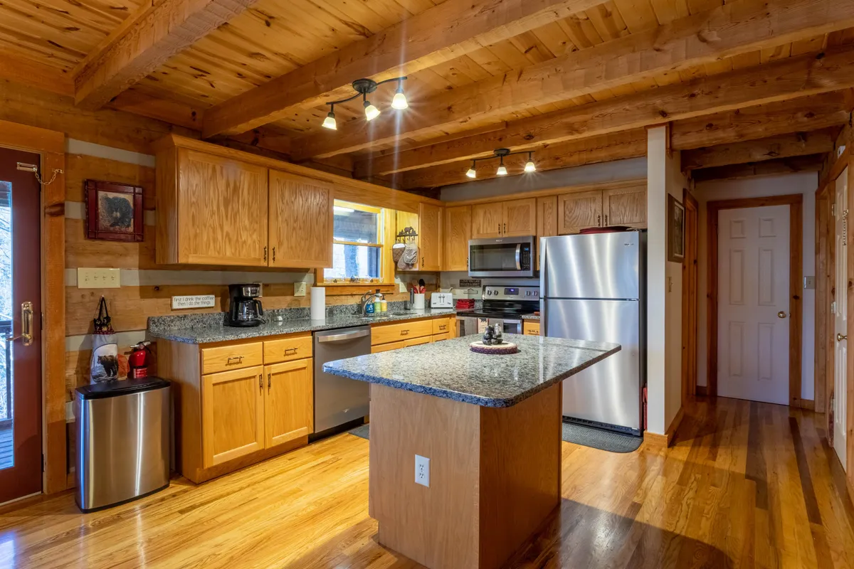 A modern kitchen area with gleaming granite countertops, stainless steel appliances, wooden cabinets, and a central island. The space is bright and inviting, ideal for cooking and gathering.