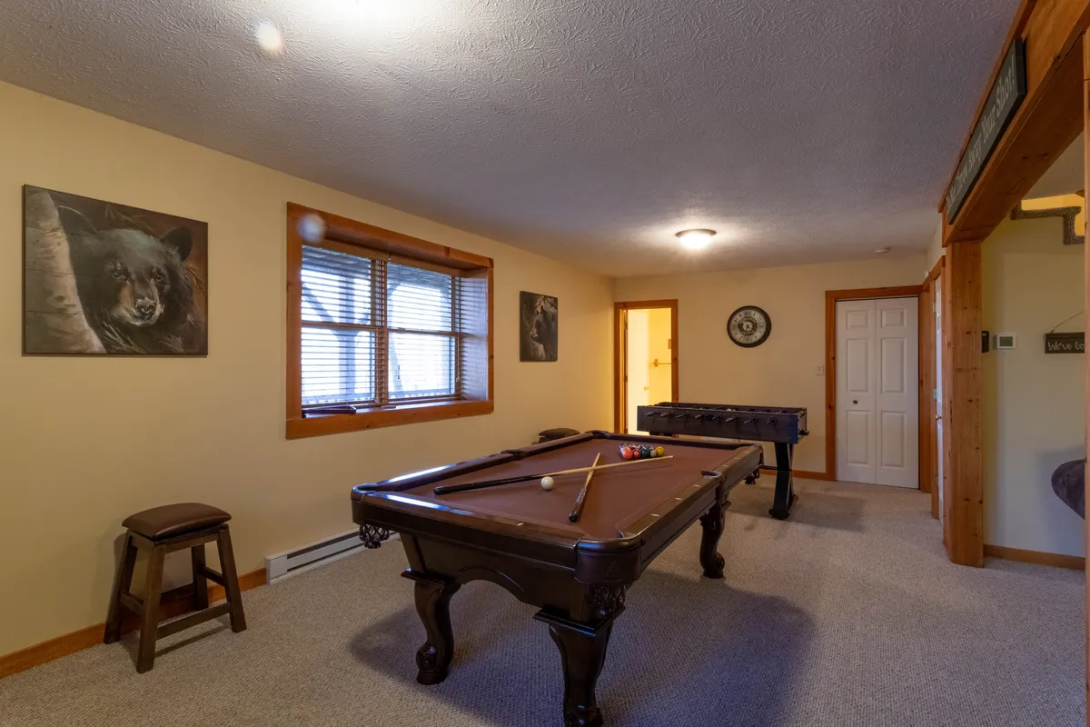 The image captures a vibrant game den with a pool table and foosball table as central features. Large windows bring in natural light, and animal artwork adds a playful touch to the space. The area has a friendly, recreational vibe, ideal for family fun and group gatherings.