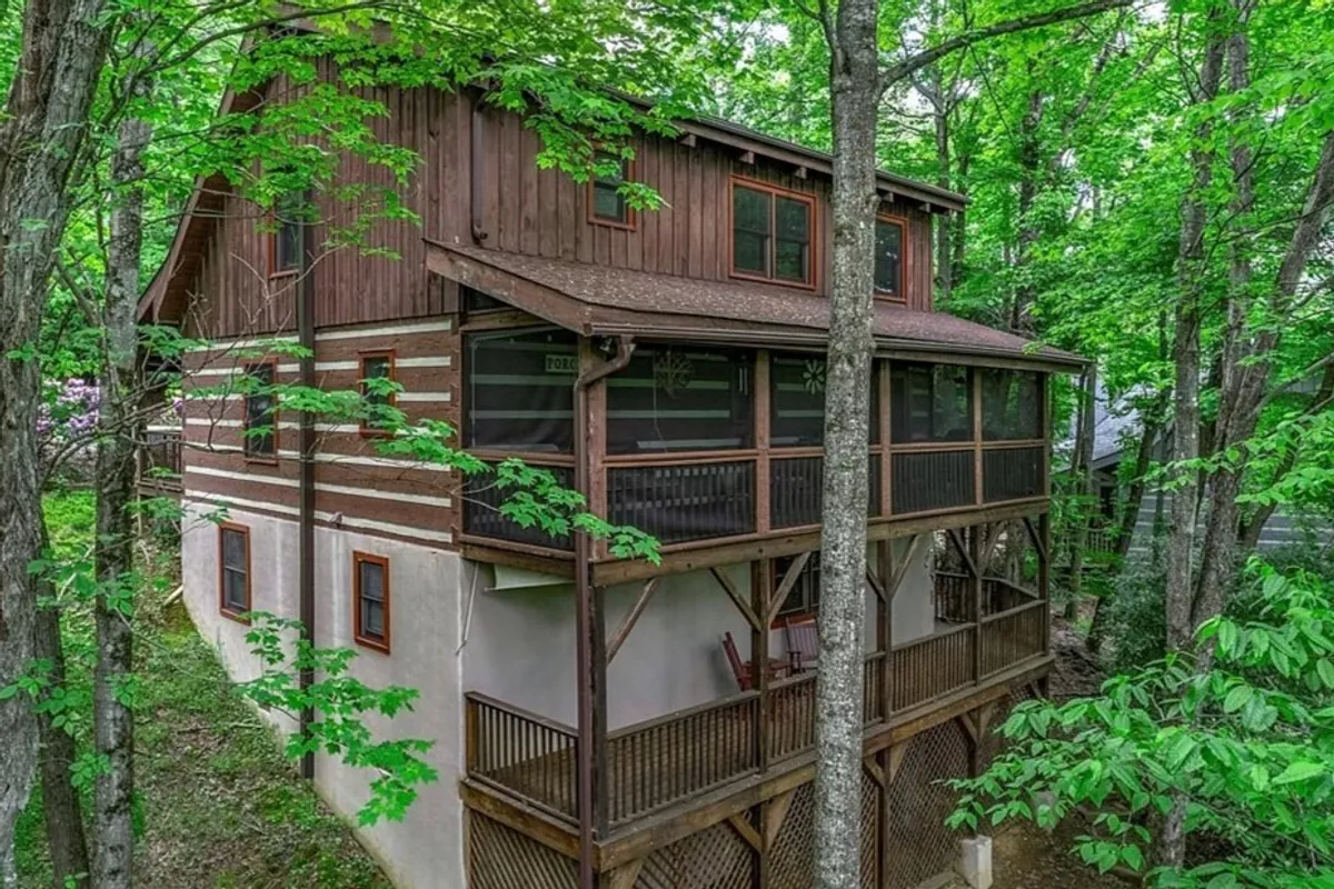 An exterior perspective featuring the home's wooden structure and expansive porches, framed by lush greenery. The porches offer spaces for relaxation, gatherings, and soaking up mountain sunsets or morning sunrises.