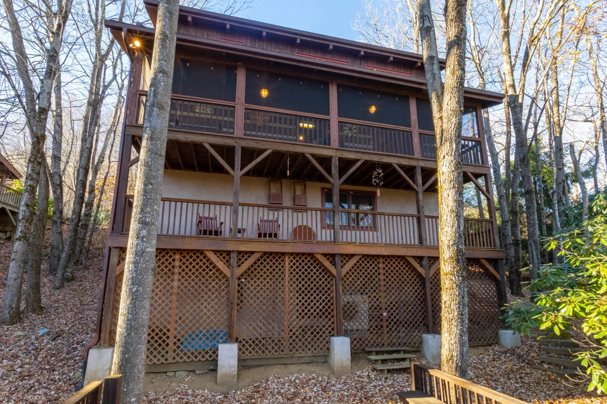A screened porch and wooden balcony nestled among the trees, offering a tranquil setting for morning coffee or evening gatherings. The space is connected to the main living areas and invites guests to savor the crisp mountain air.