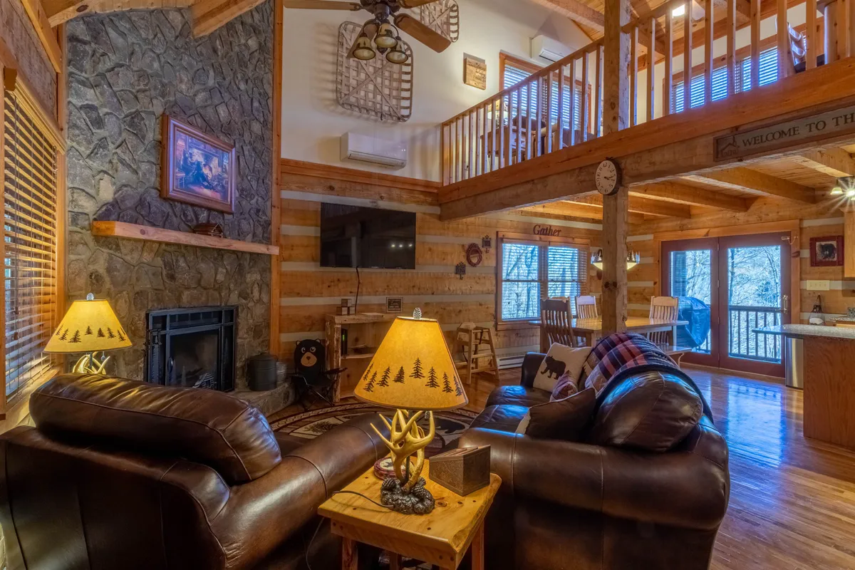 A cozy interior scene focused on a stone fireplace, leather sofas, wooden beams, and decorative lamps. The arrangement invites family gatherings and relaxing moments after a day outdoors, particularly in winter.